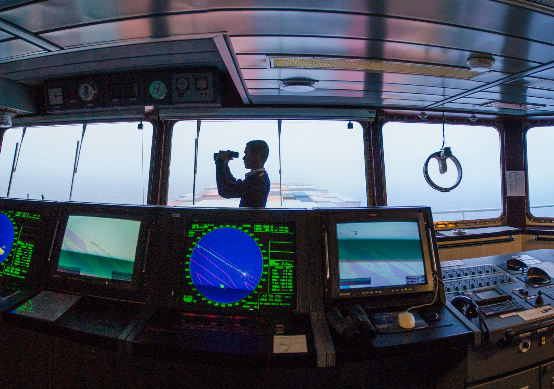 navigator on cargo ship bridge using binoculars