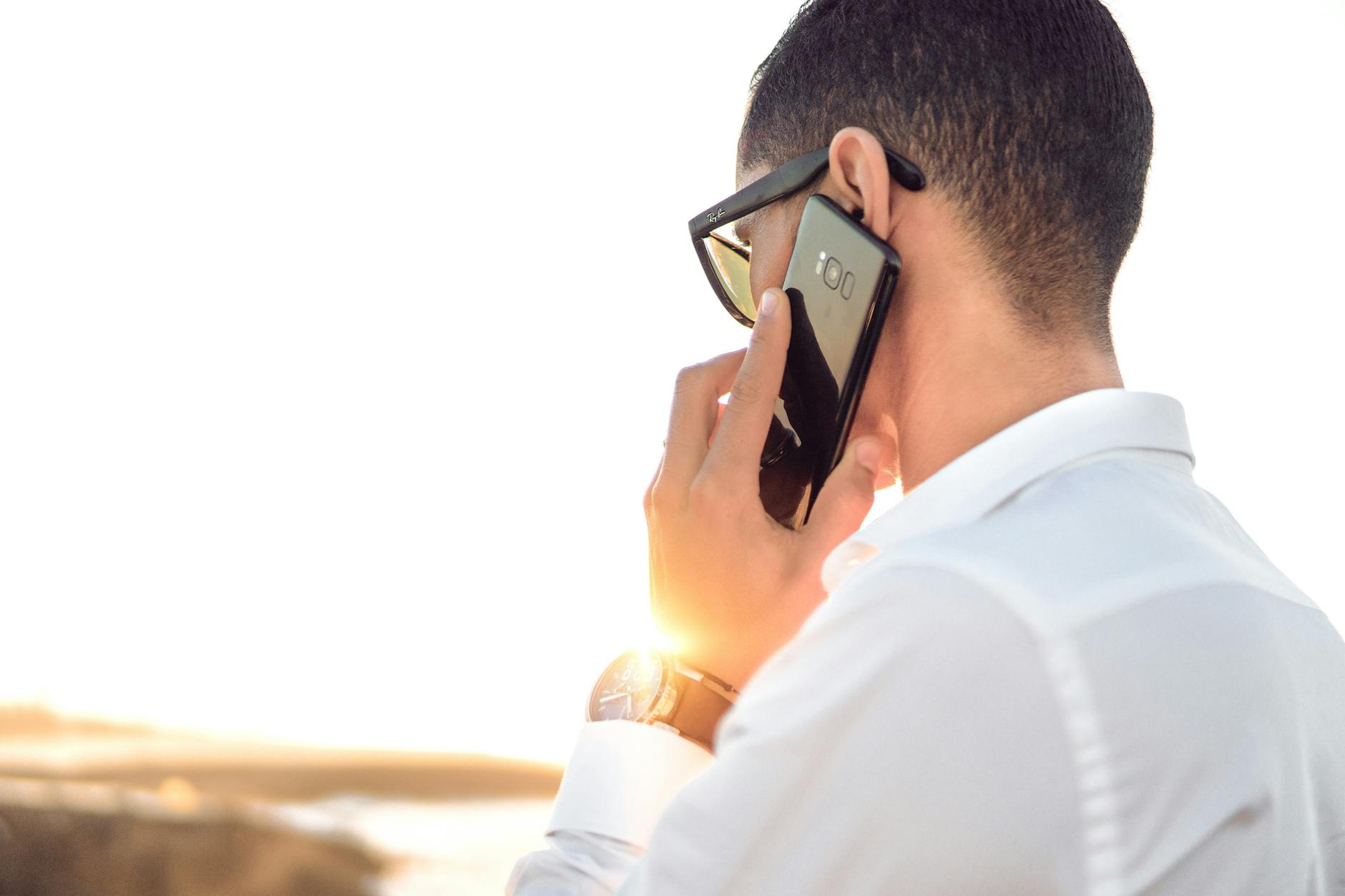 shallow focus photography of a man in white collared dress shirt talking to the phone using black android smartphone