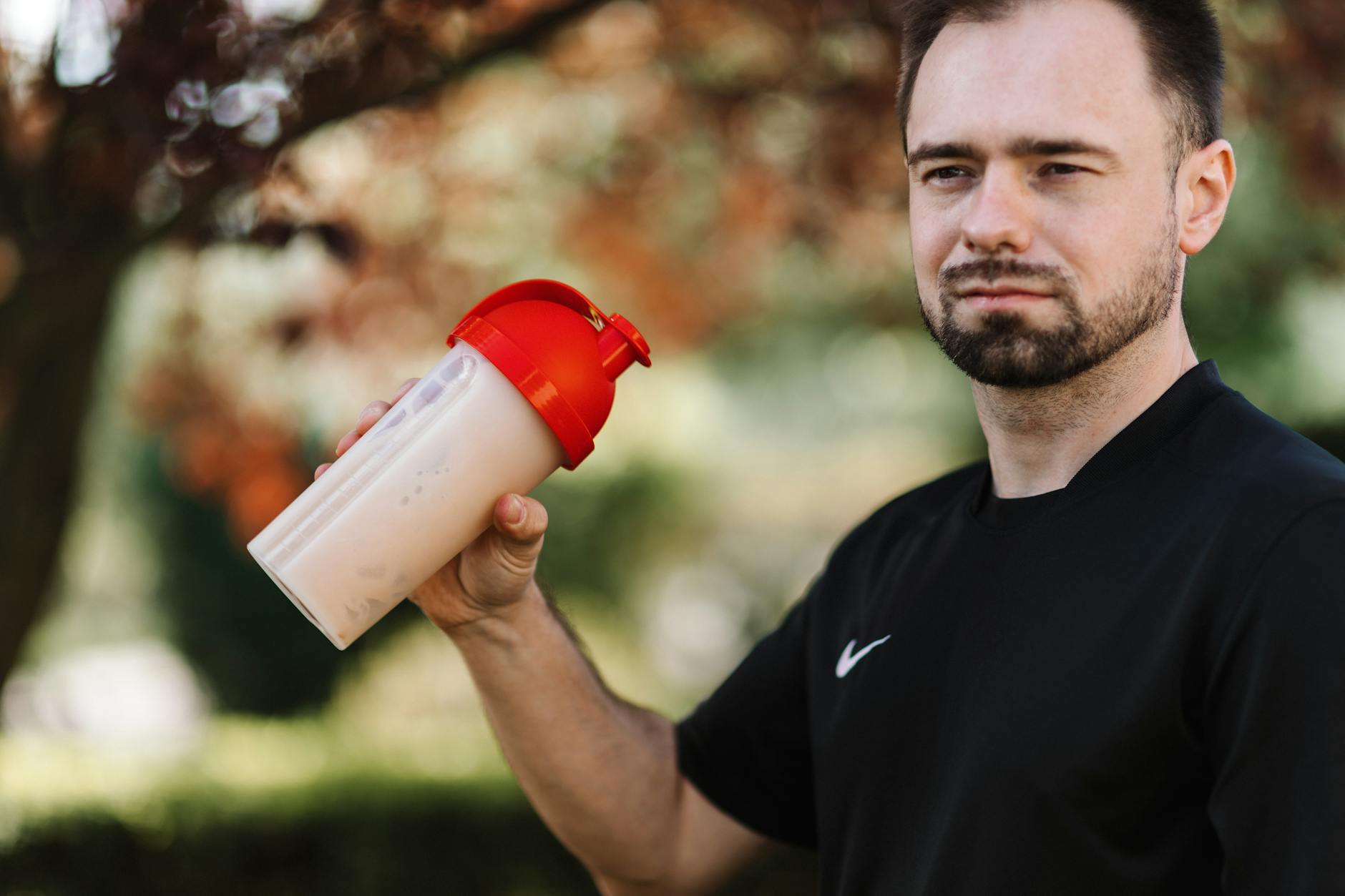 a bearded man holding a plastic tumbler with red lid